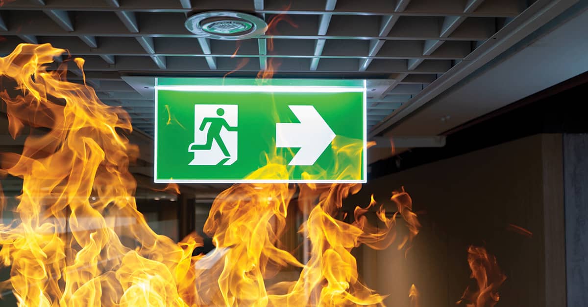 Green fire escape sign hanging on the ceiling in the office with flames underneath