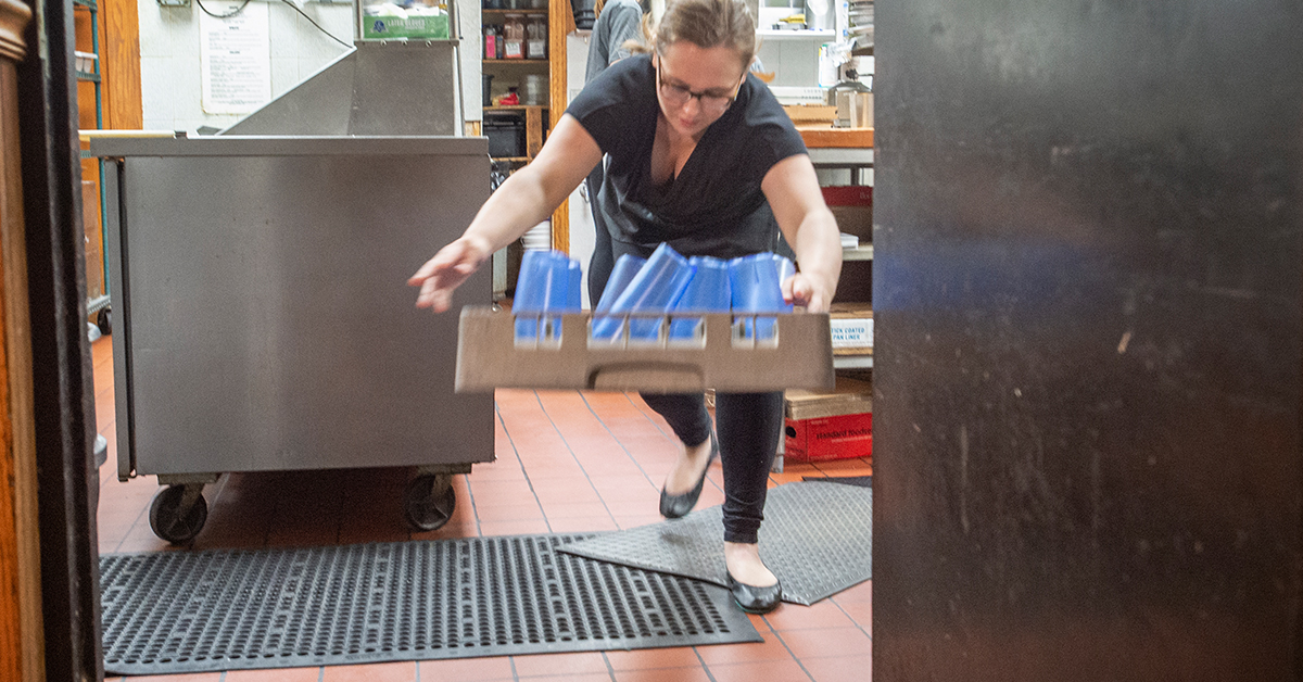 Restaurant worker carrying tray of cups tripping over a mat
